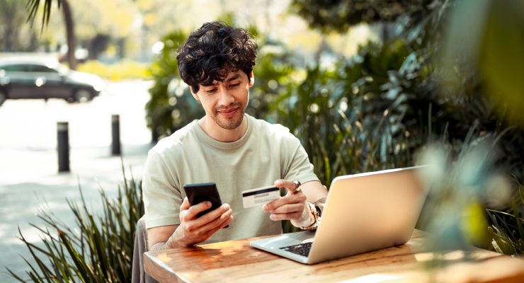 Man sitting outside with laptop and phone checking balance on his gift card