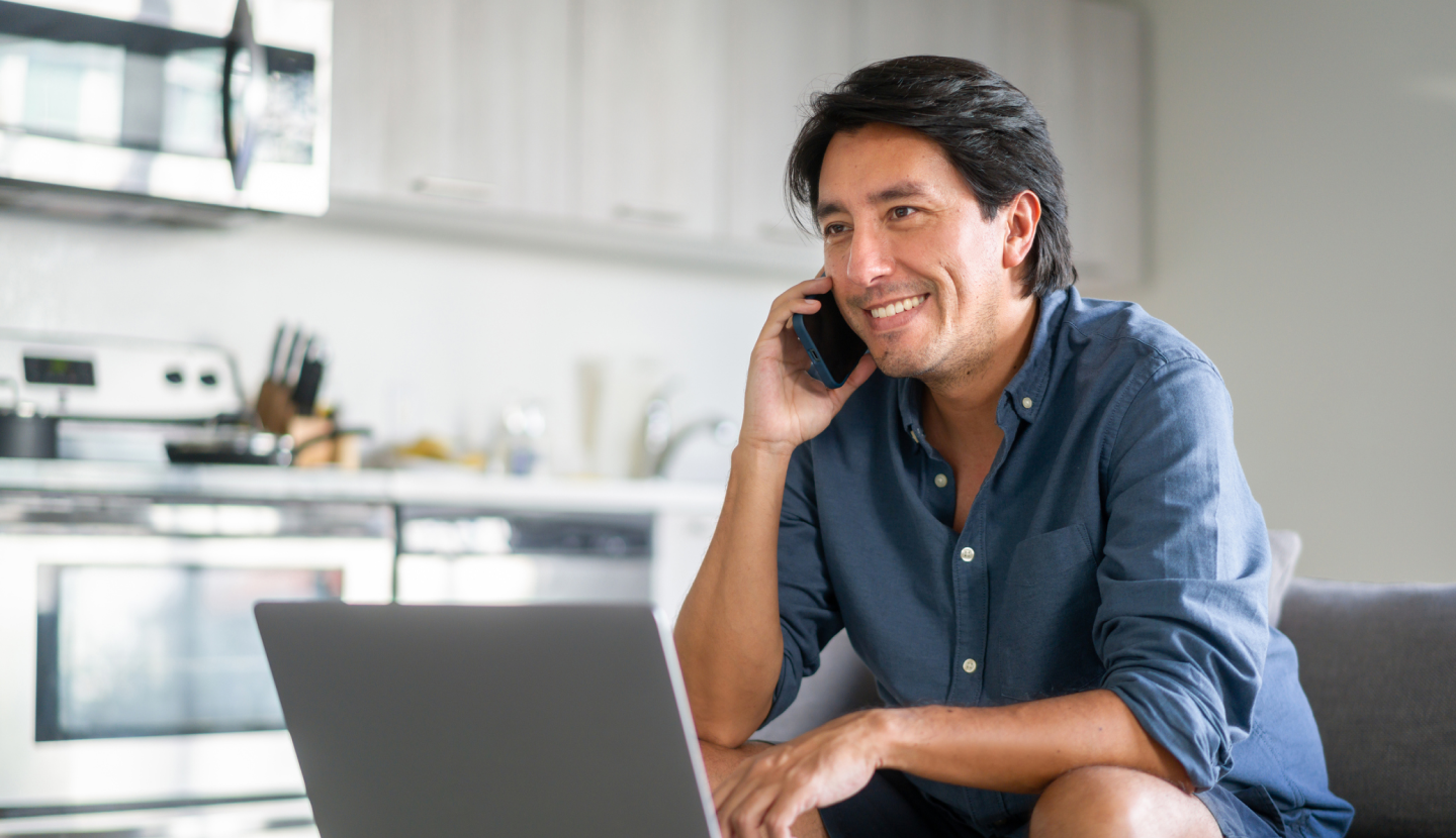 A man sitting on his couch, smiling while talking on the phone 