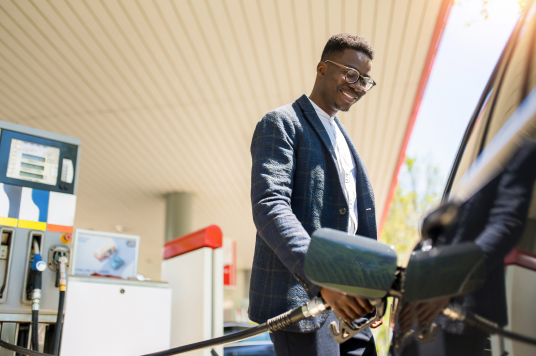 Tall man wearing a suit, standing at gas station pump filling up his car's gas tank