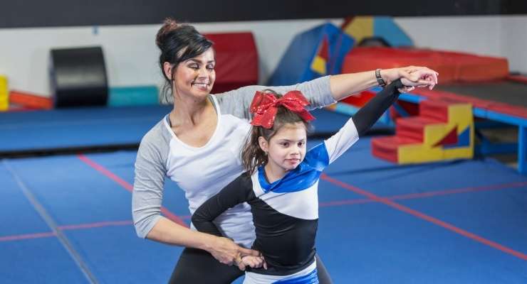 coach teaches a young child how to make a cheerleading pose