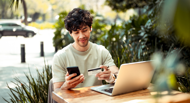 Man sitting outside with laptop and phone checking balance on his gift card